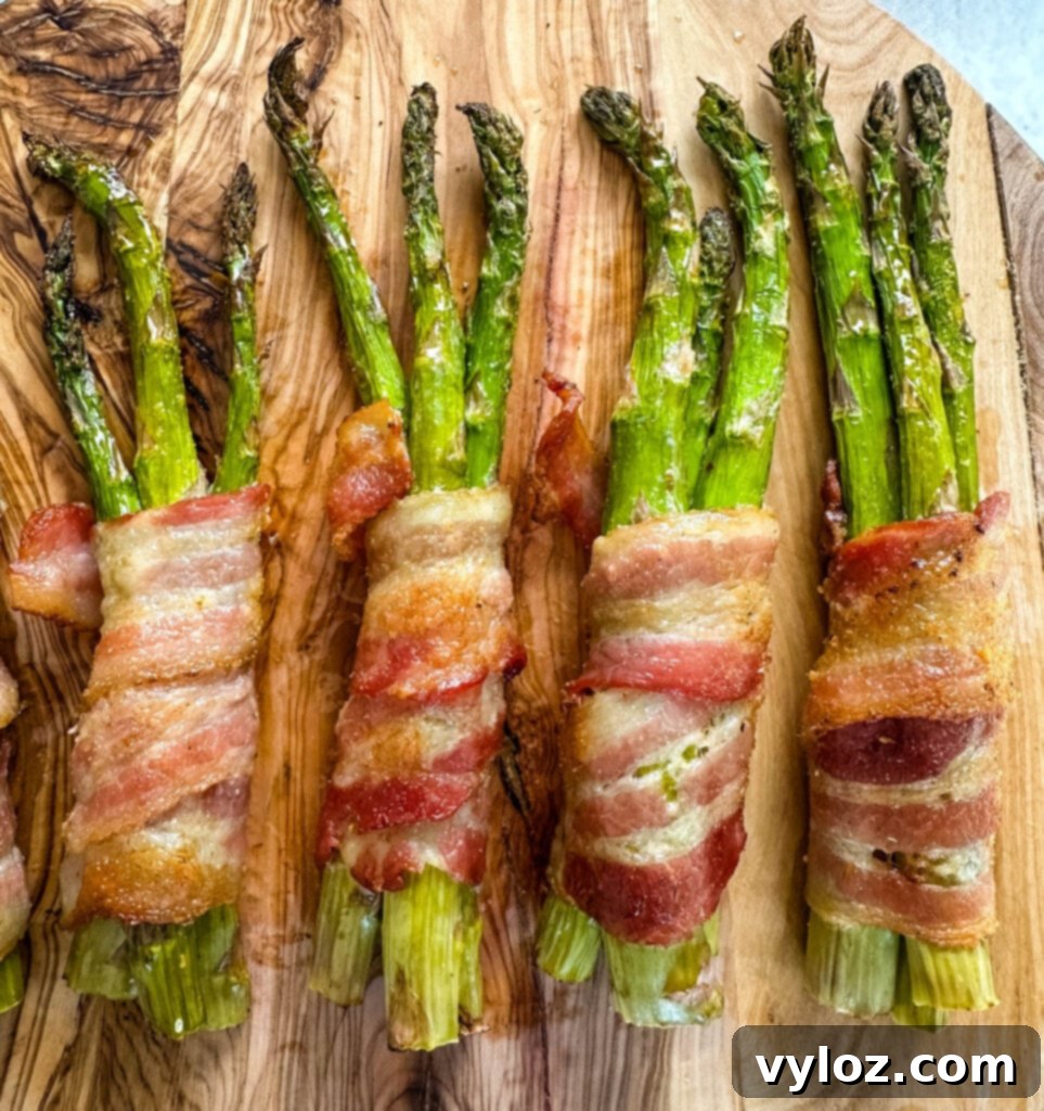 A serving of air fryer bacon wrapped asparagus on a wooden cutting board with a fork