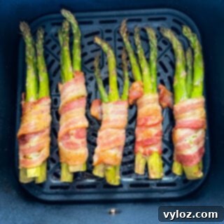 Cooked bacon wrapped asparagus, golden and crispy, in an air fryer basket
