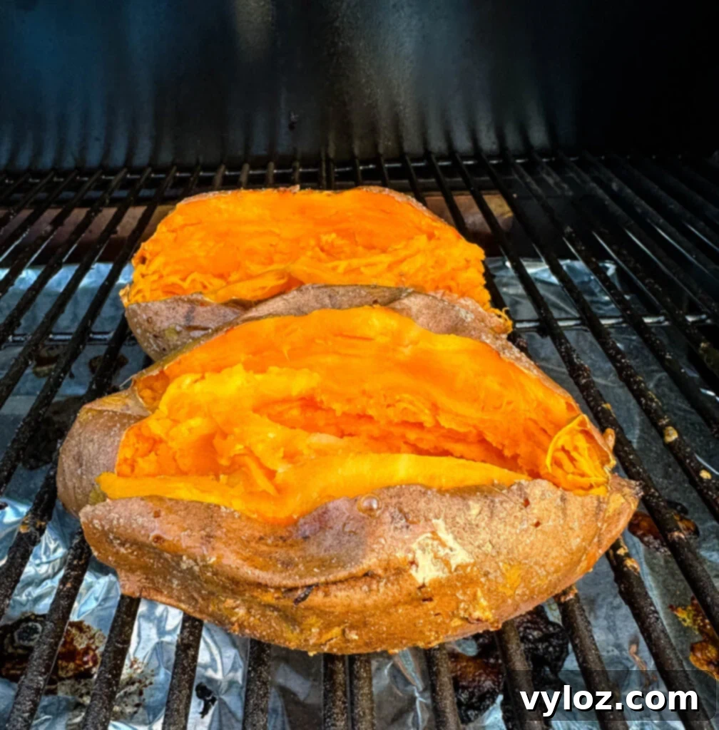 Close-up of sweet potatoes on a smoker grill with visible smoke.