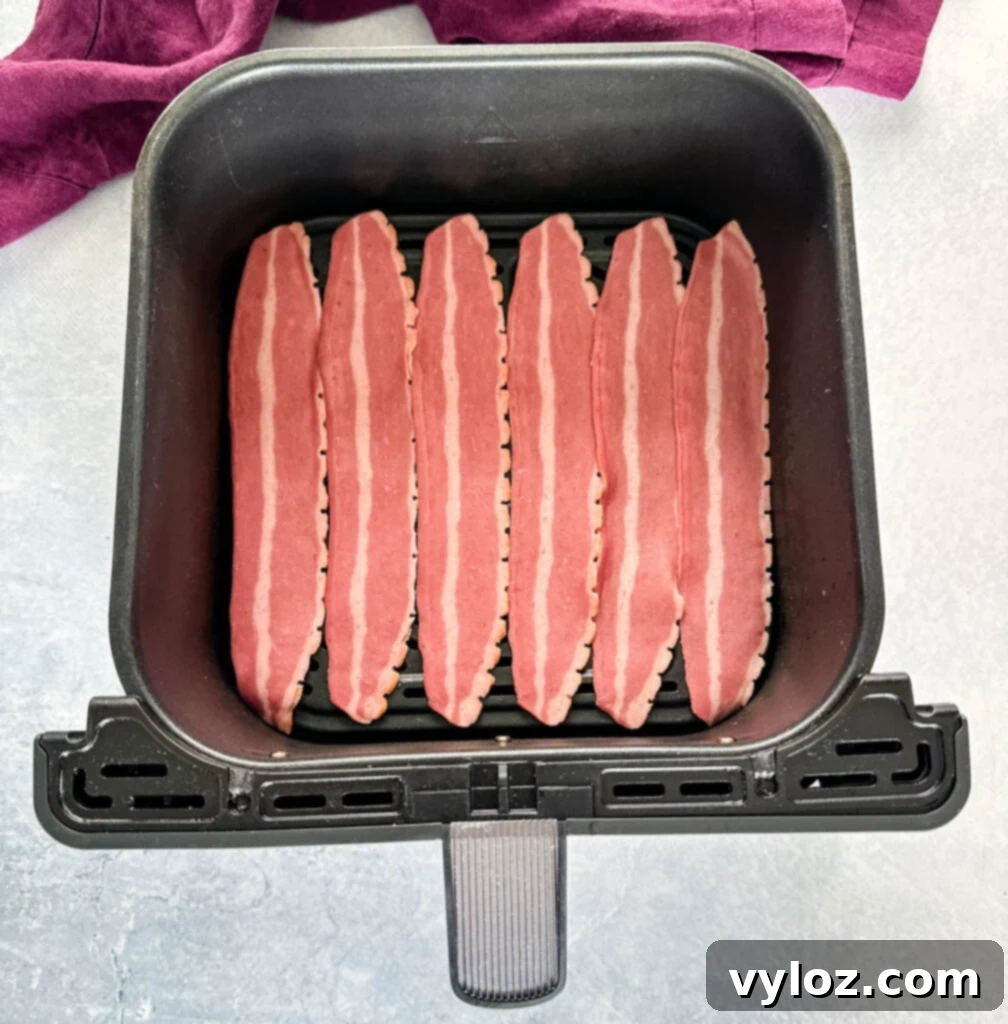 Turkey bacon strips cooking in an air fryer basket, halfway through the crisping process.
