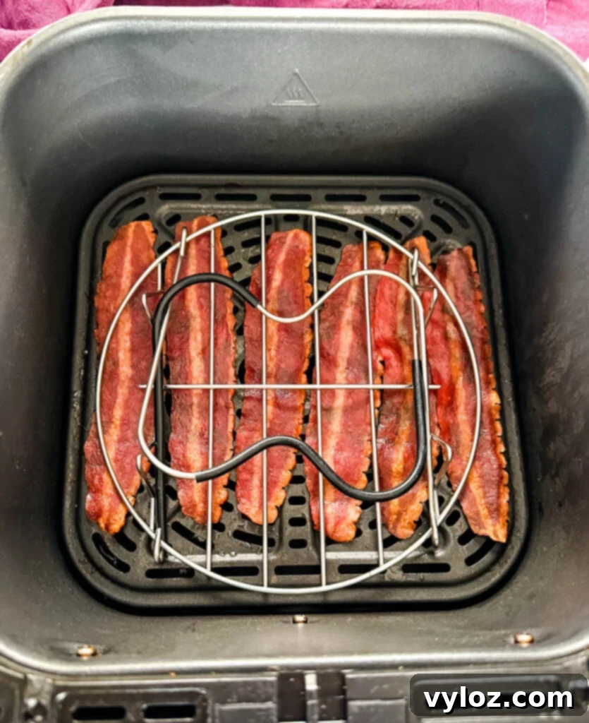 Perfectly cooked, flat turkey bacon strips in an air fryer basket, held down by a metal trivet for even crisping.