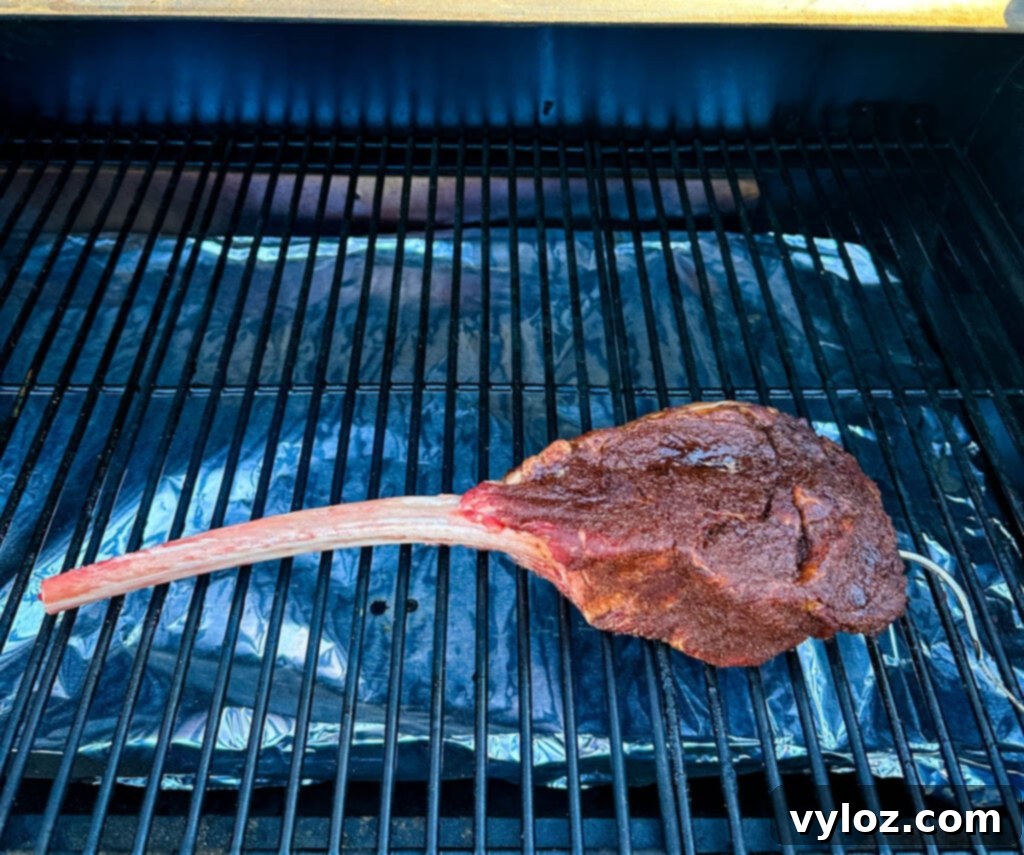 raw seasoned tomahawk steak with butter on a Traeger pellet grill