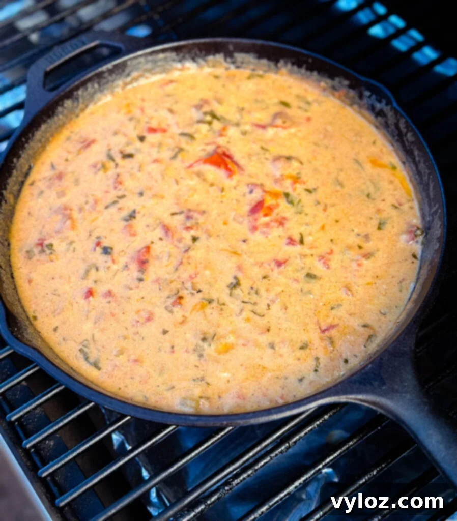 Smoked queso cheese dip in a cast iron skillet on a Traeger smoker grill, surrounded by smoke