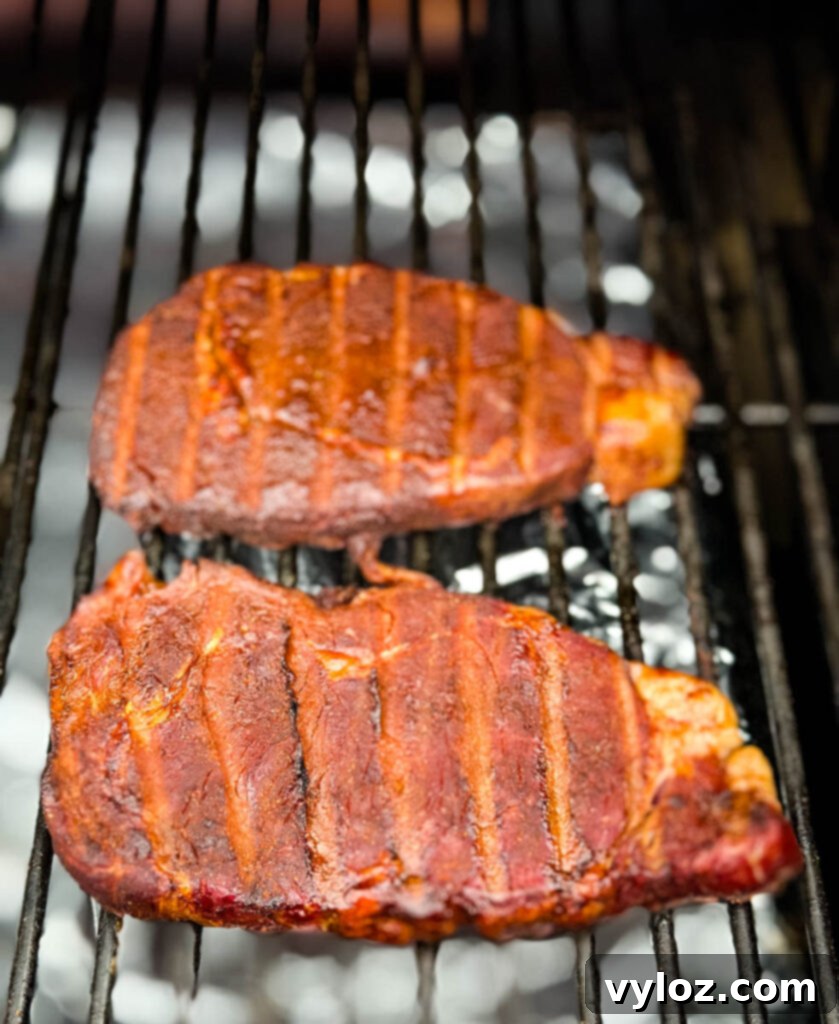 Traeger Wood Fired Ribeye 6 Smoked ribeyes cooking on a Traeger smoker grill, showing a rich, developing crust.
