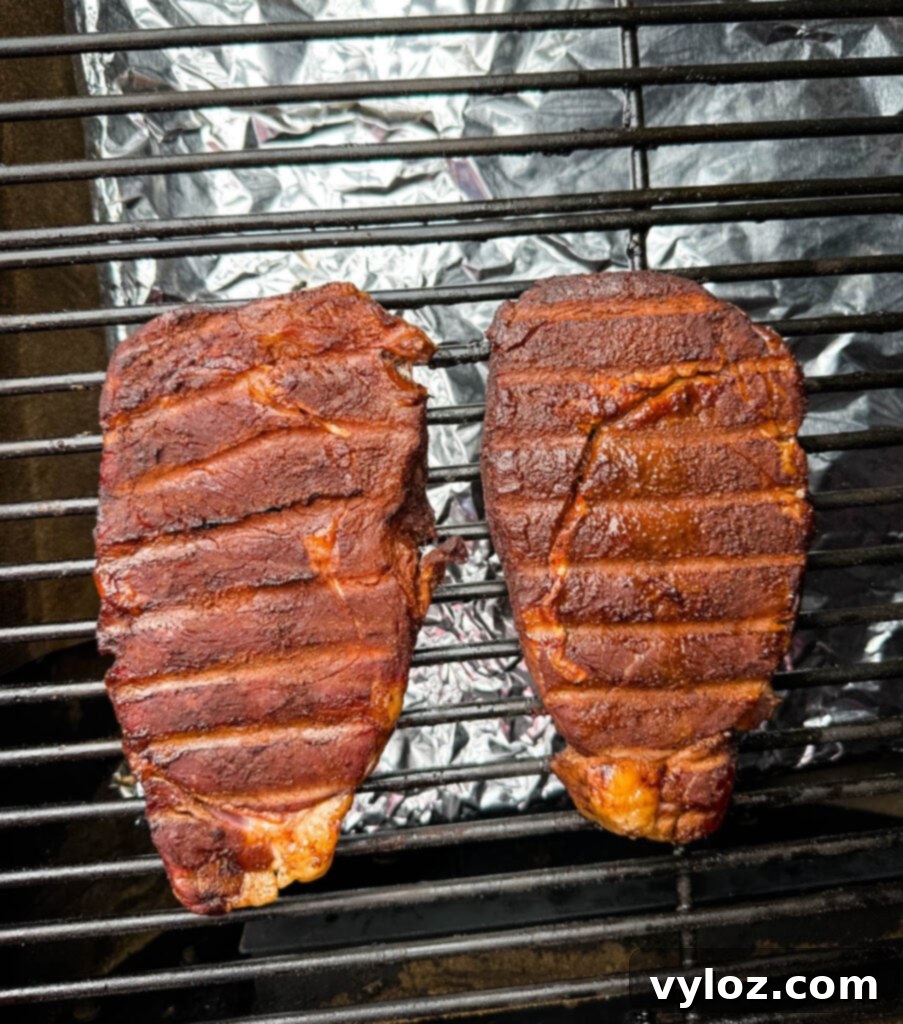 Traeger Wood Fired Ribeye 7 Smoked ribeyes cooking on a Traeger smoker grill, showing beautiful char and smoke ring development.
