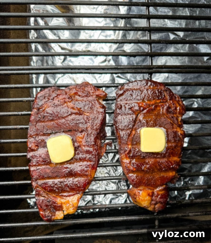 Traeger Wood Fired Ribeye 8 Smoked ribeyes on a Traeger smoker grill, glistening with melted butter, nearing completion.