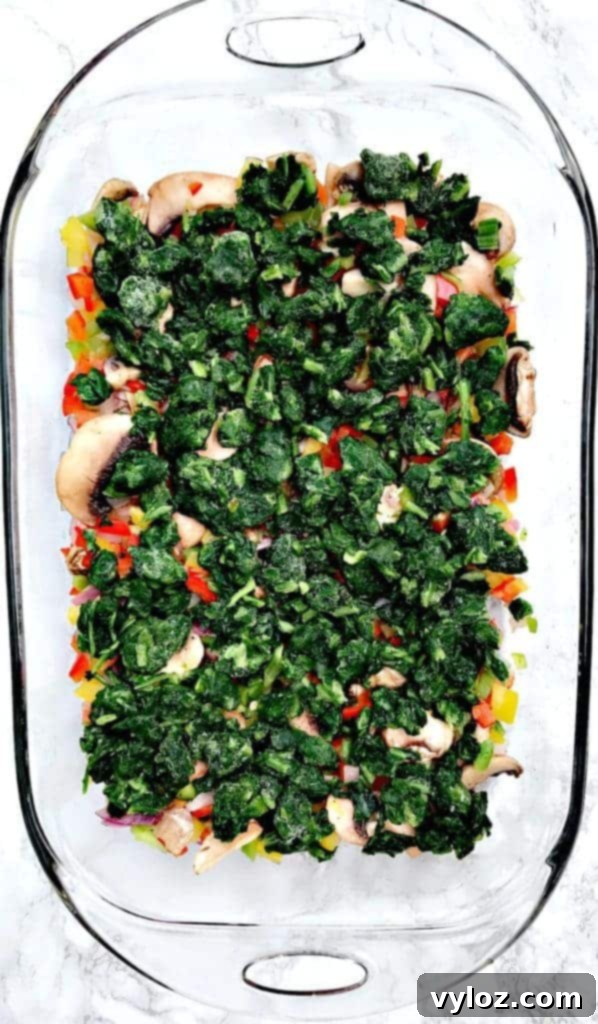 Preparation step for Low-Carb Bacon, Egg, and Spinach Breakfast Casserole, showing various vegetable ingredients in a glass pan before cooking