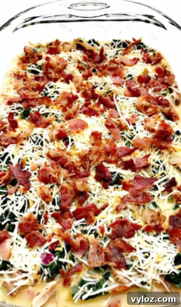 Top view of bacon, cheese, and vegetable ingredients for Low-Carb Bacon, Egg, and Spinach Breakfast Casserole in a glass pan before baking