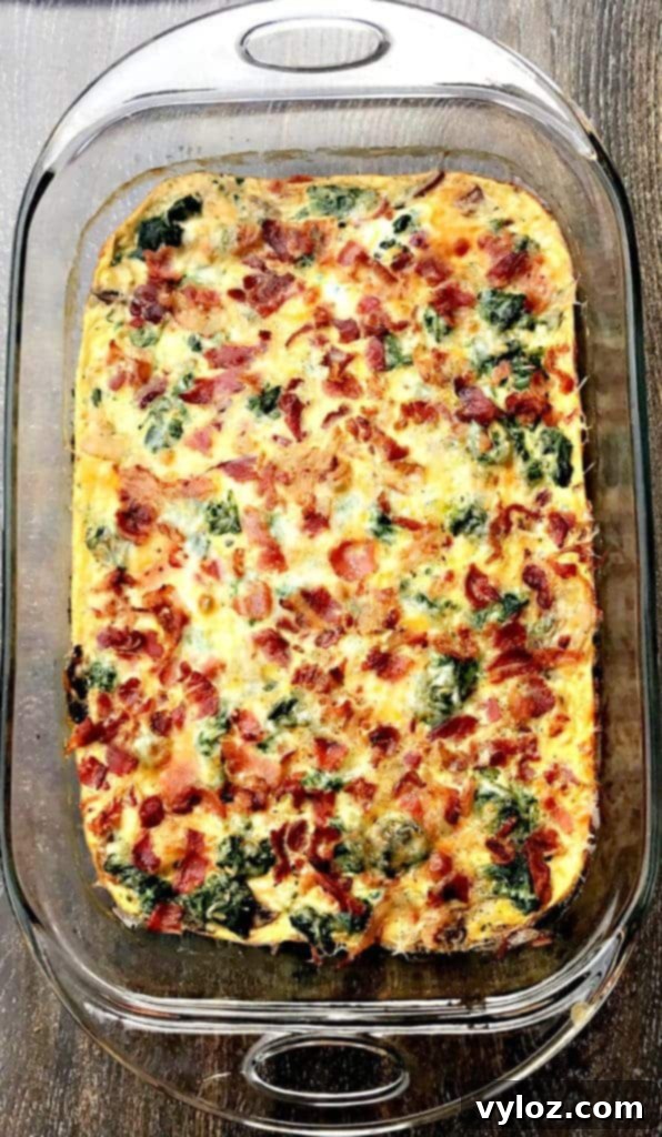 Fully cooked Low-Carb Bacon, Egg, and Spinach Breakfast Casserole in a glass pan on a brown surface, golden brown and ready to be served