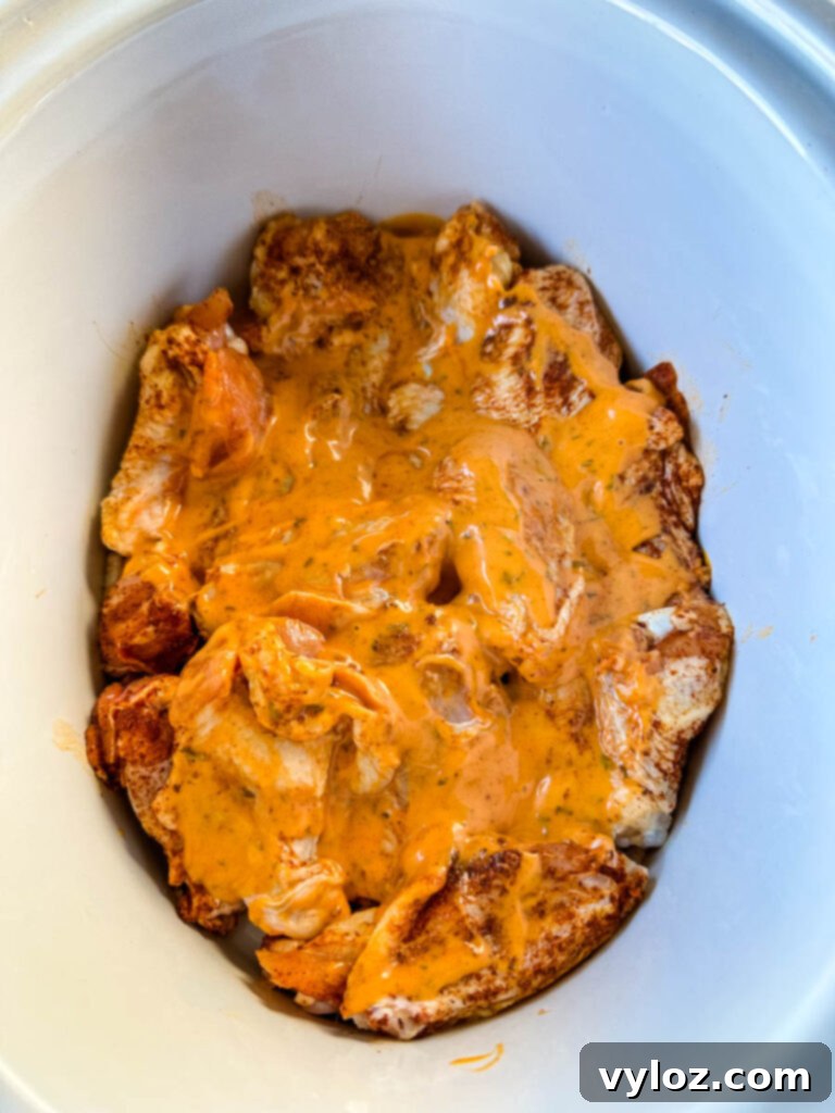 raw seasoned chicken wings in a Crockpot slow cooker drizzled with buffalo sauce