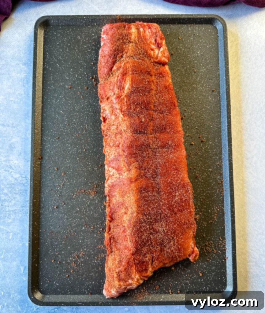 Slow Cooker BBQ Spare Ribs 6 A rack of raw pork ribs, perfectly seasoned with a dry rub, resting on a sheet pan