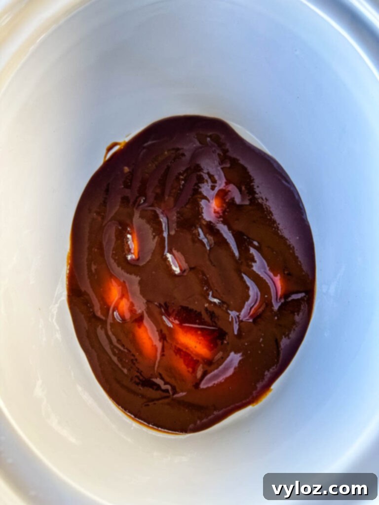 Slow Cooker BBQ Spare Ribs 7 A generous layer of BBQ sauce being poured directly into a Crockpot slow cooker, ready for the ribs