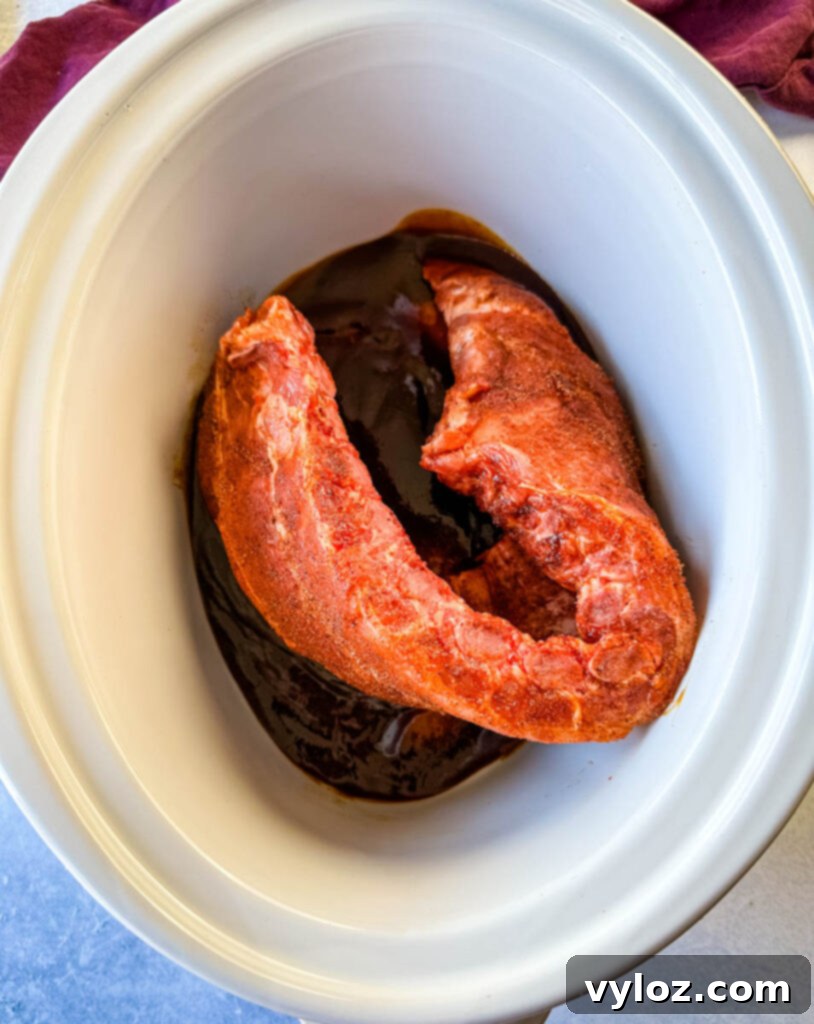 Slow Cooker BBQ Spare Ribs 8 Seasoned ribs nestled in a Crockpot slow cooker, generously coated with BBQ sauce, ready for cooking