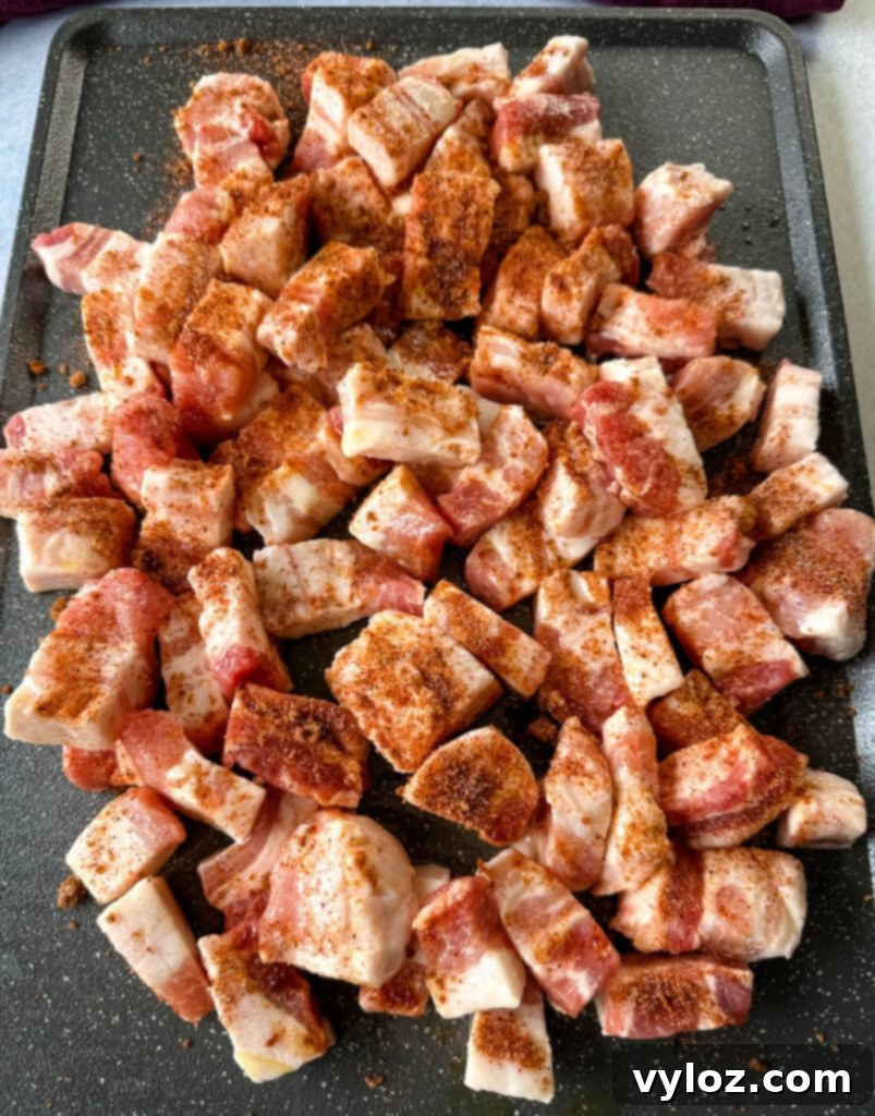 raw seasoned pork belly cut into chunks on a sheet pan