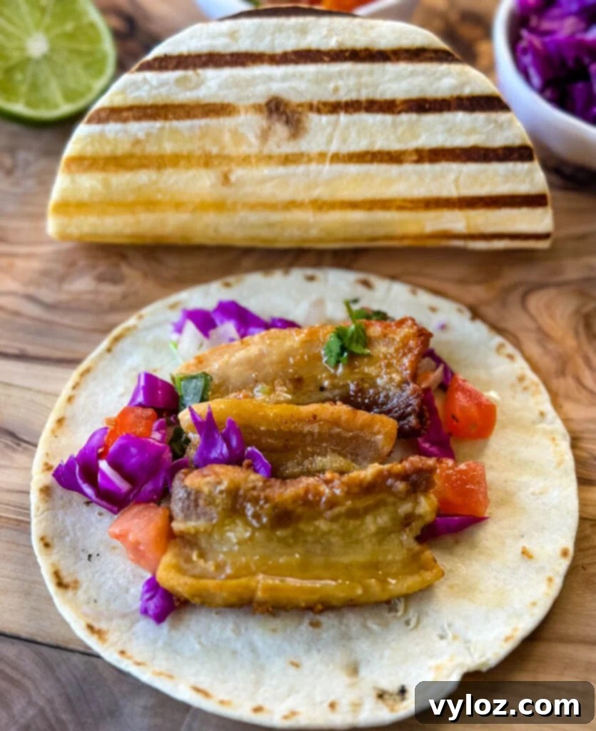 Close-up of a crispy pork belly taco featuring seared flour tortilla, spicy Chipotle sauce, and fresh pico de gallo