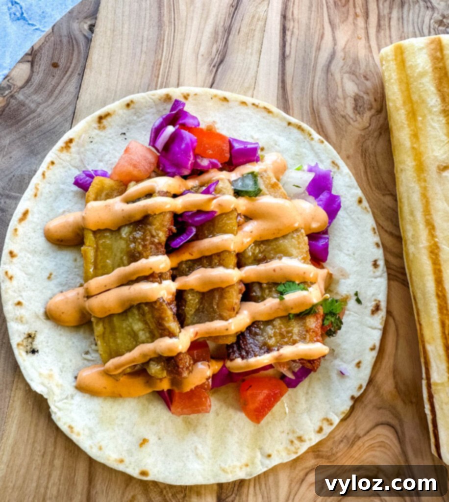 A beautifully assembled pork belly taco with a seared flour tortilla, spicy Chipotle sauce, and pico de gallo