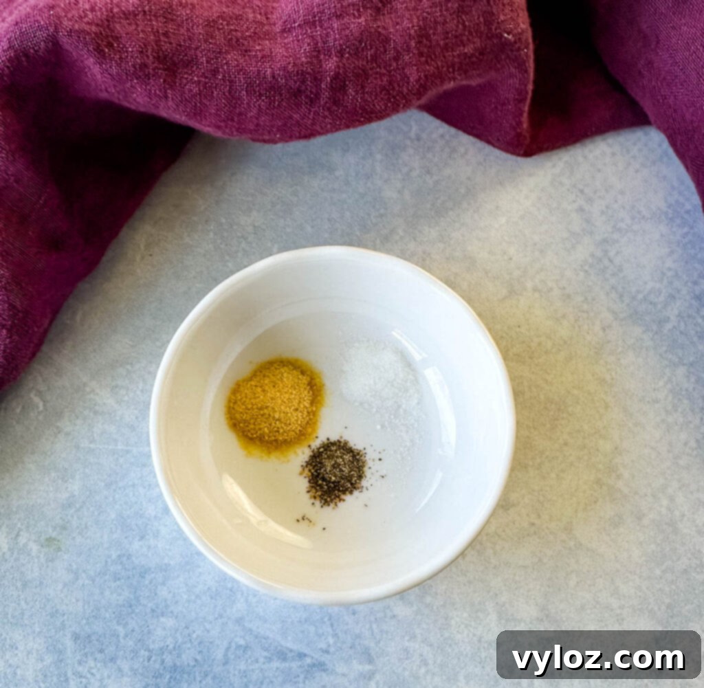 A small white bowl containing a mix of dried seasonings: garlic powder, salt, and black pepper, essential for balancing the dressing's flavors.