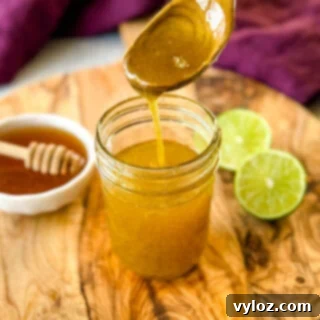 A spoonful of freshly prepared honey lime salad dressing lifted above a glass jar, demonstrating its perfect consistency.
