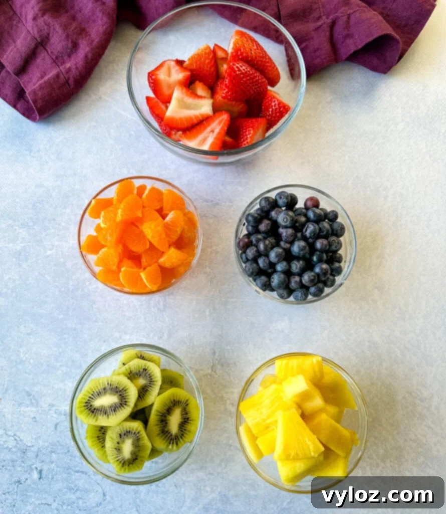 Refreshing Rainbow Fruit Medley 3 A collection of vibrant, fresh fruits, including sliced strawberries, mandarin oranges, kiwi slices, plump blueberries, and pineapple chunks, neatly arranged in separate glass bowls, ready for a delicious fruit salad.