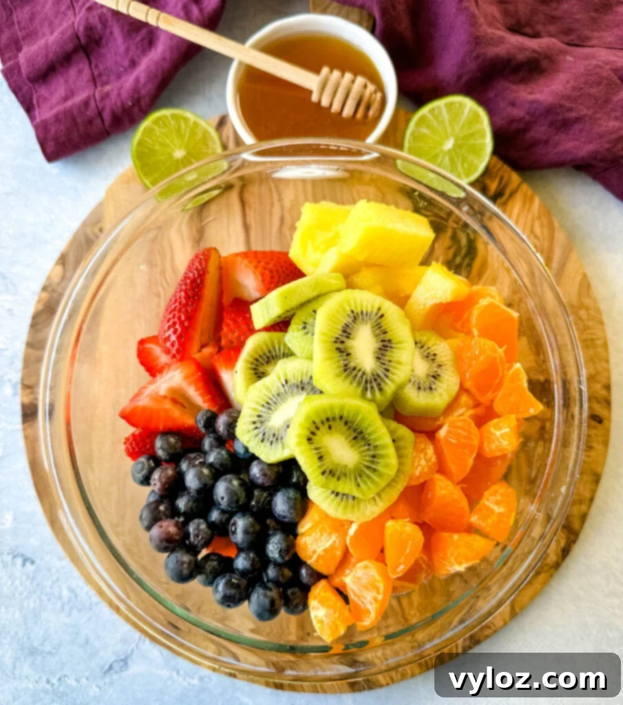 Refreshing Rainbow Fruit Medley 4 A colorful and fresh assortment of strawberries, mandarin oranges, kiwi, blueberries, and pineapple chunks, perfectly mixed in a clear glass bowl, showcasing the vibrant 'rainbow' of fruits.