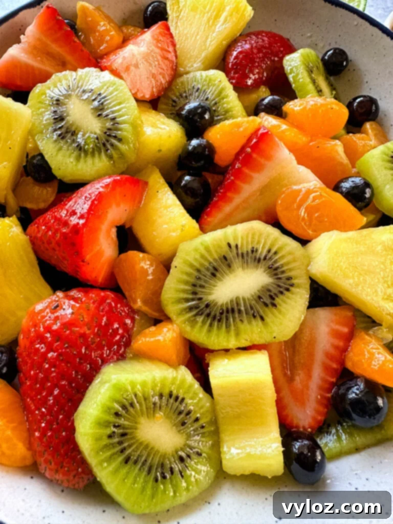Refreshing Rainbow Fruit Medley 6 A close-up of a generously sized white bowl filled with a delightful medley of fresh strawberries, mandarin oranges, kiwi slices, blueberries, and pineapple chunks, all glistening with honey lime dressing.