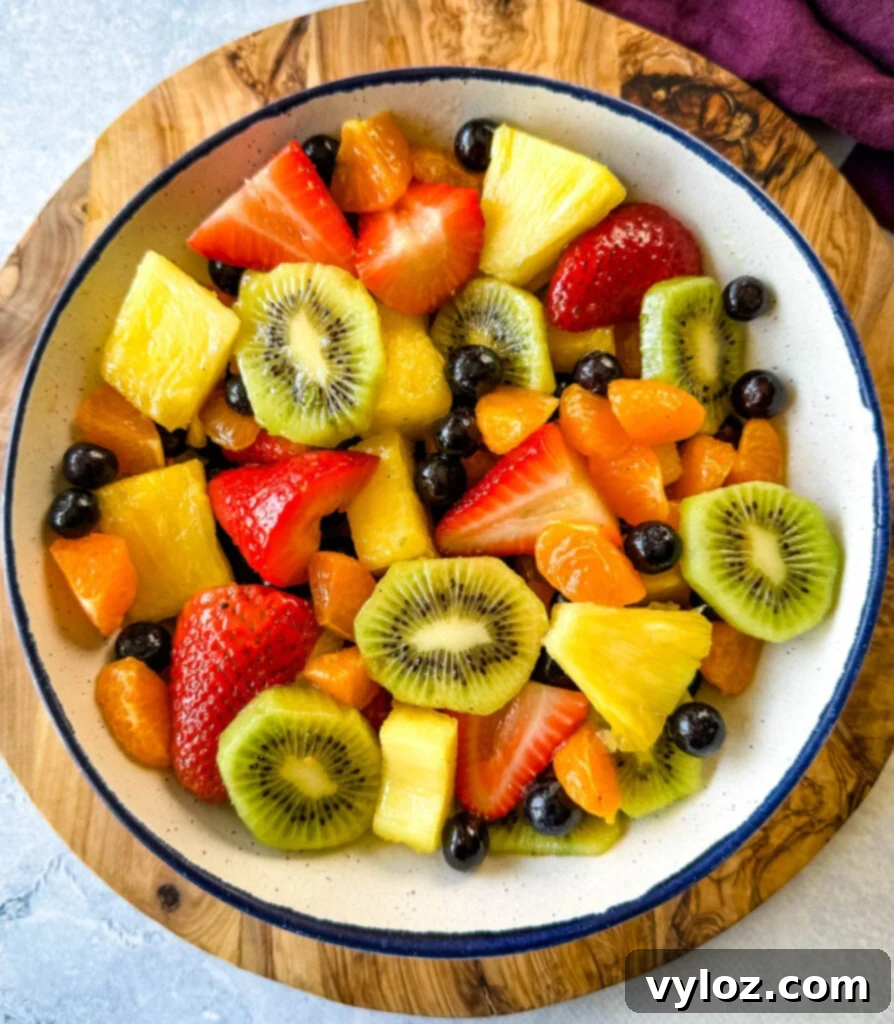 Refreshing Rainbow Fruit Medley 7 An appetizing view of a fresh fruit salad, featuring a vibrant mix of strawberries, mandarin oranges, kiwi, blueberries, and pineapple, arranged beautifully in a white bowl with a hint of honey lime dressing.