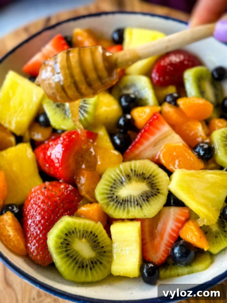 Refreshing Rainbow Fruit Medley 9 A beautifully presented fruit salad featuring an array of fresh strawberries, mandarin oranges, kiwi, blueberries, and pineapple, glistening with honey lime dressing in a crisp white bowl.