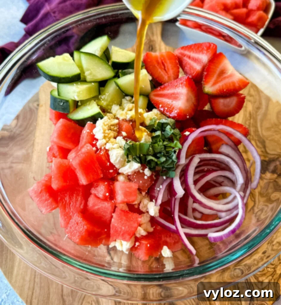 Vibrant Watermelon Feta Salad with Balsamic 7 watermelon salad with feta, cucumbers, avocado, basil, strawberries, onion, and balsamic lime dressing in a glass bowl drizzled with balsamic dressing