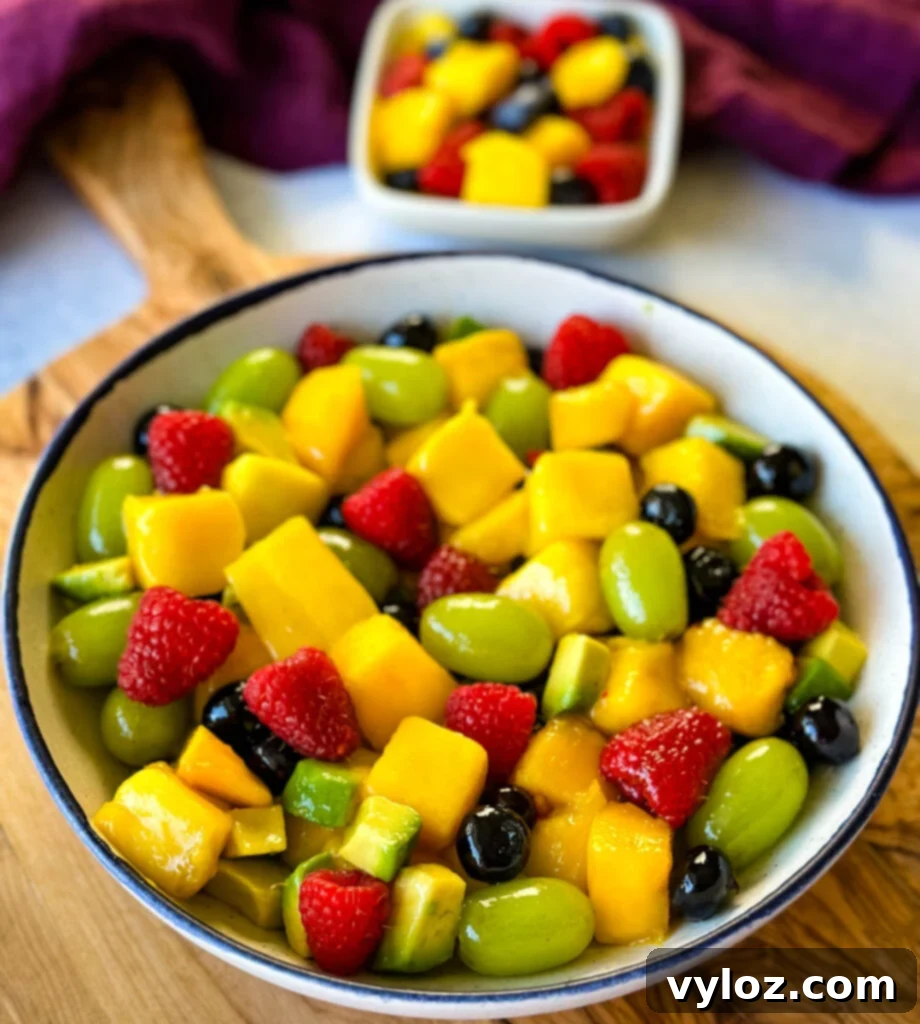 Tropical Mango Medley with Zesty Lime Honey Dressing 2 Vibrant mango fruit salad with raspberries, blueberries, grapes, and avocado in a white bowl, beautifully drizzled with honey-lime dressing, ready to be served.