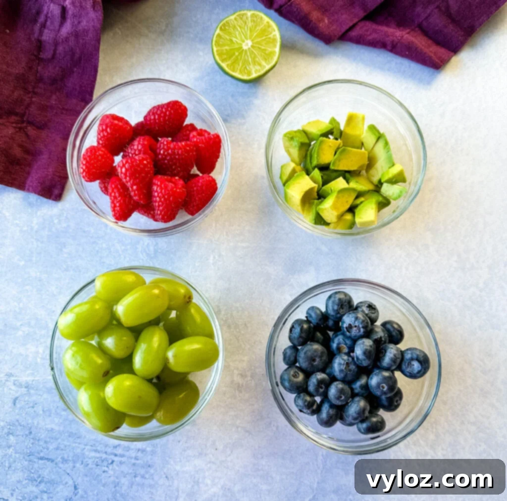 Tropical Mango Medley with Zesty Lime Honey Dressing 4 Individual bowls holding fresh lemon, vibrant raspberries, plump blueberries, crisp green grapes, and perfectly diced avocado, meticulously arranged on a rustic wooden board, ready for fruit salad assembly.