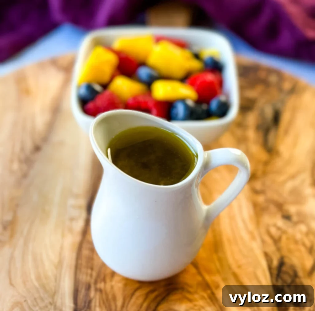 Tropical Mango Medley with Zesty Lime Honey Dressing 5 Ingredients for homemade honey lime dressing, including honey, lime, and olive oil, alongside a colorful assortment of fresh fruits on a wooden cutting board, ready for the fruit salad.