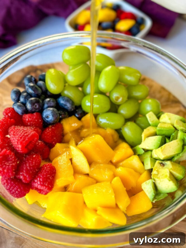 Tropical Mango Medley with Zesty Lime Honey Dressing 7 Beautifully presented mango fruit salad with raspberries, blueberries, grapes, and avocado in a clear glass bowl, generously drizzled with glossy honey-lime dressing, highlighting its vibrant colors.