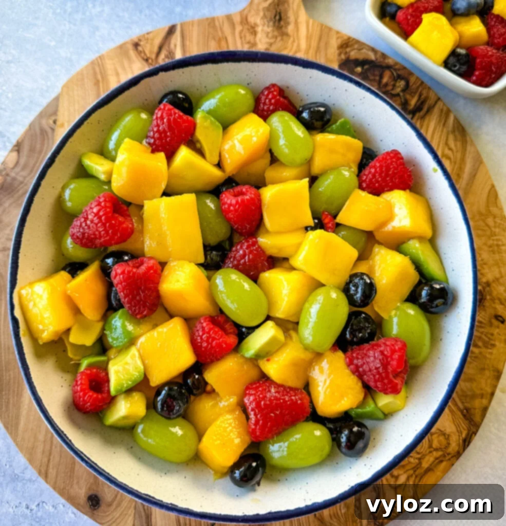 Tropical Mango Medley with Zesty Lime Honey Dressing 8 An inviting, perfectly styled mango fruit salad featuring raspberries, blueberries, grapes, and avocado, served in a pristine white bowl.