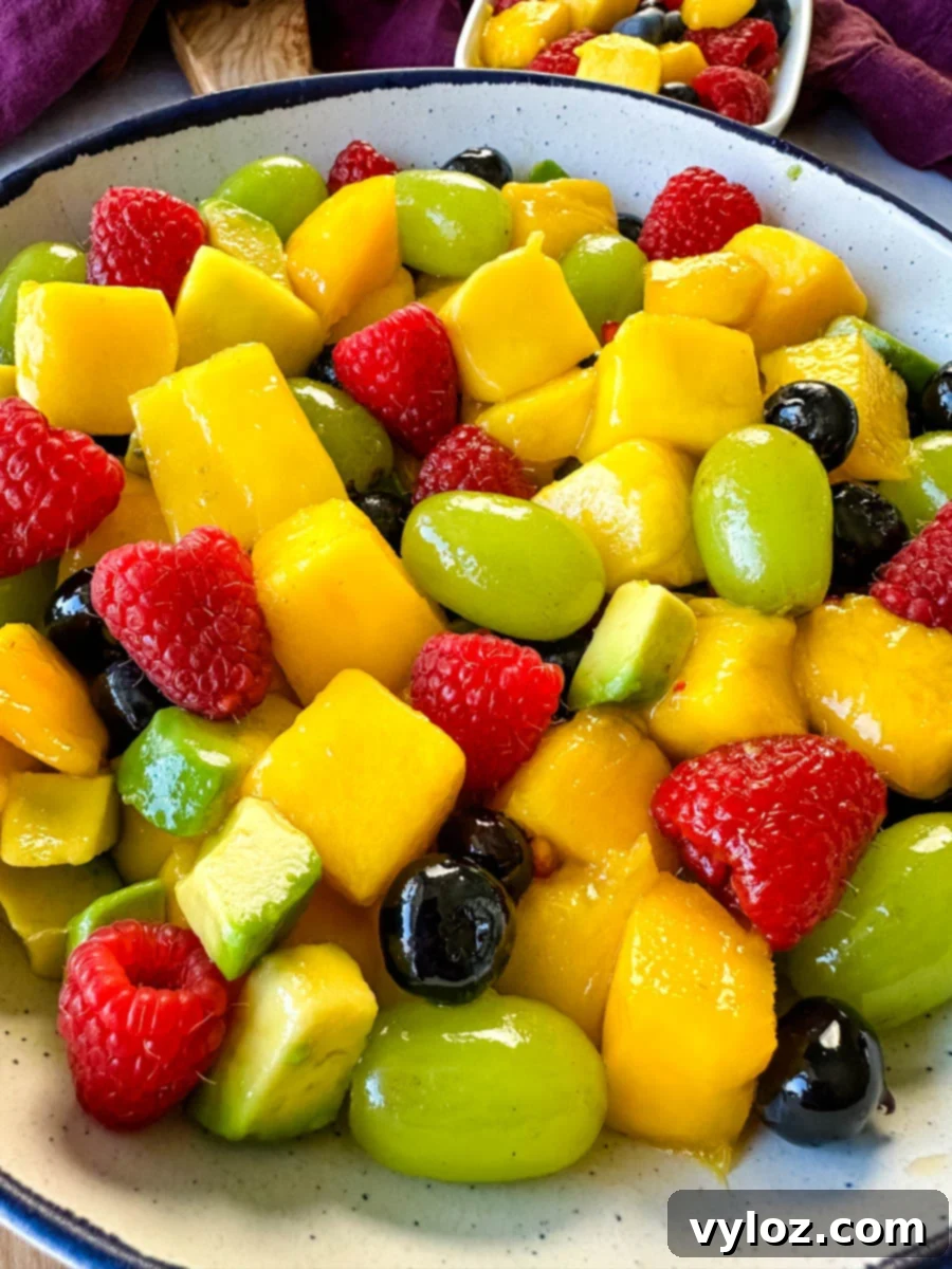 Tropical Mango Medley with Zesty Lime Honey Dressing 9 A large, beautifully composed mango fruit salad, brimming with raspberries, blueberries, grapes, and creamy avocado, presented in a crisp white bowl.