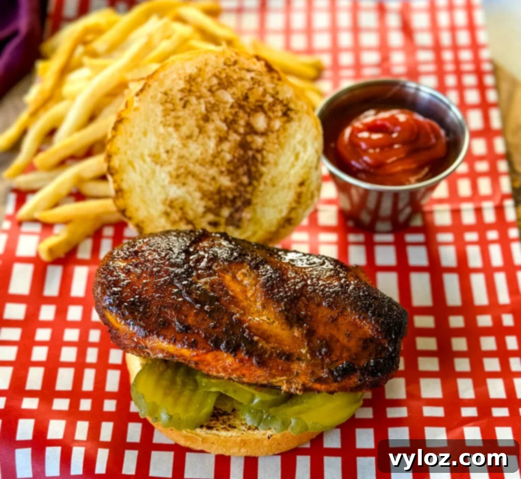 blackened chicken sandwich on a bun on a plate with fries