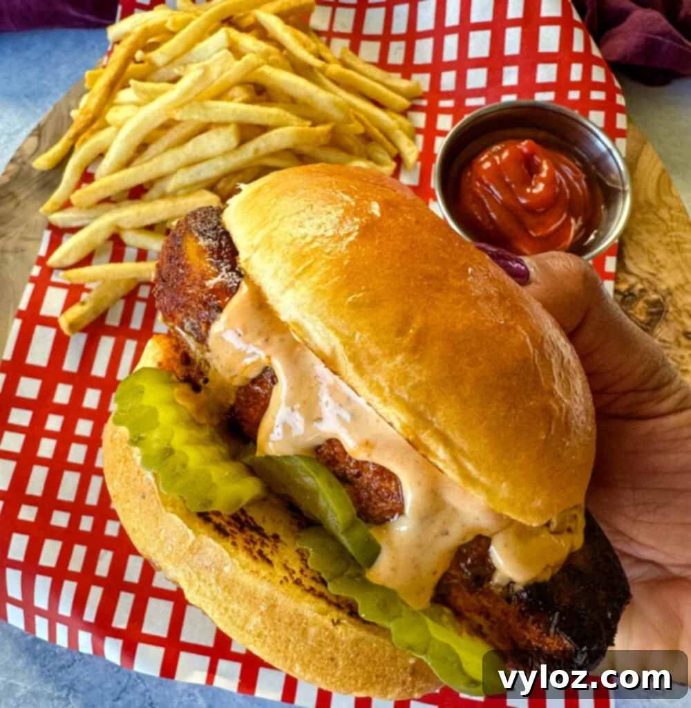 person holding blackened chicken sandwich on a bun with spicy mayo on a plate with fries