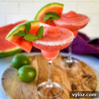 Frozen watermelon margaritas in a sugar rimmed lined glass with fresh watermelon and limes