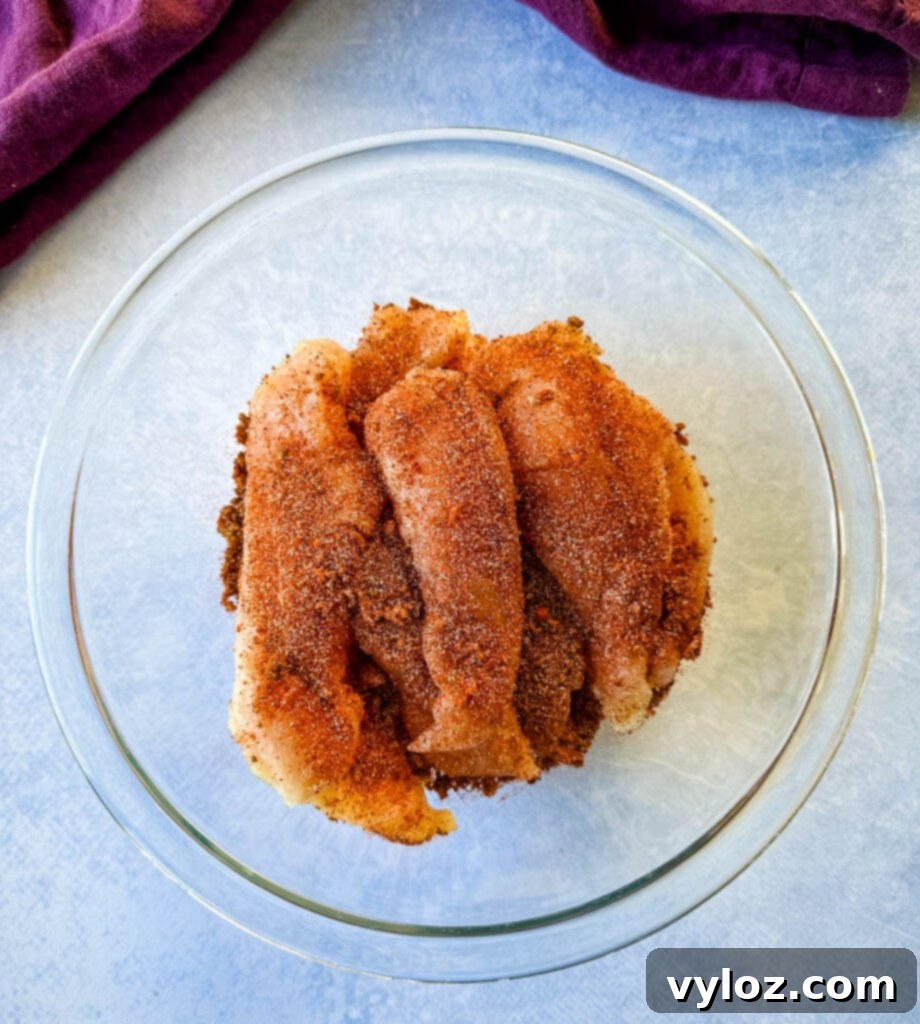 raw seasoned chicken tenders in a glass bowl, glistening with rub