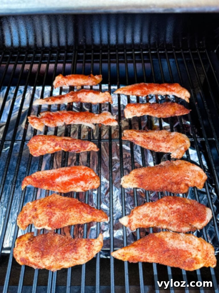 raw seasoned chicken tenders on a Traeger smoker grill, evenly spaced