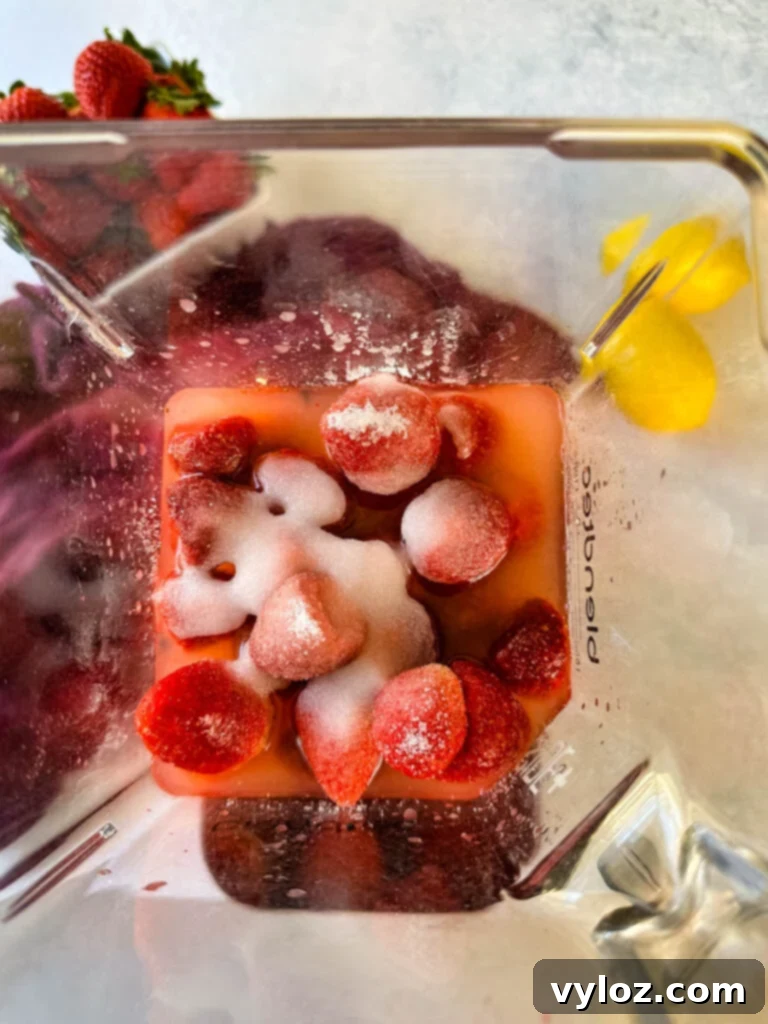 Frozen strawberries, sweetener, lemon juice, and ice in a blender, ready to be blended.