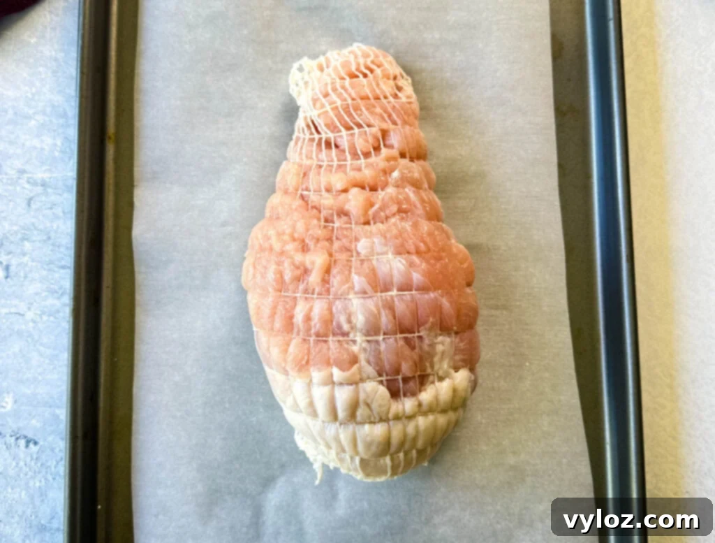 raw, seasoned boneless turkey breast wrapped in a net on a parchment paper lined sheet pan
