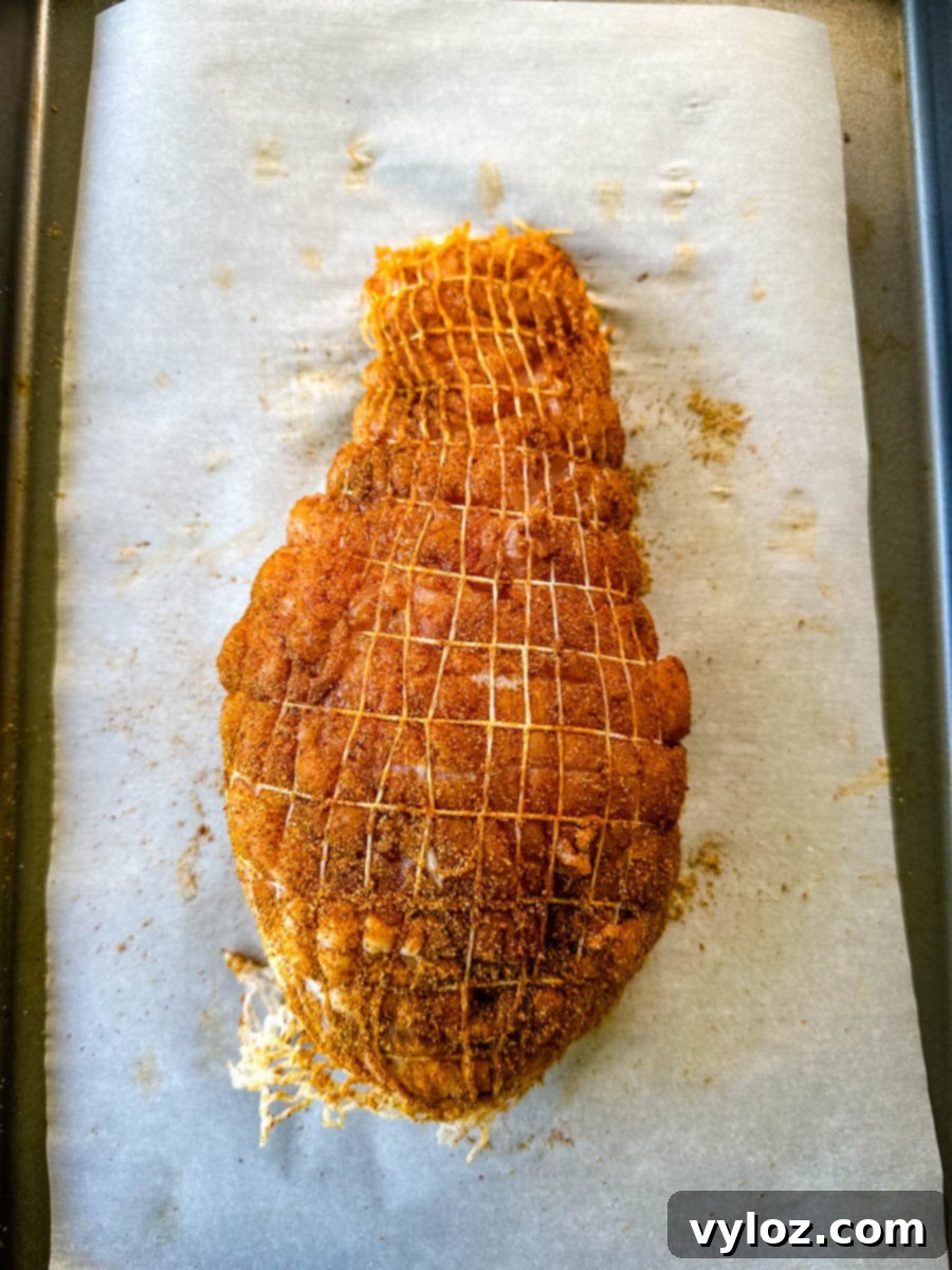 raw, seasoned boneless turkey breast wrapped in a net on a parchment paper lined sheet pan