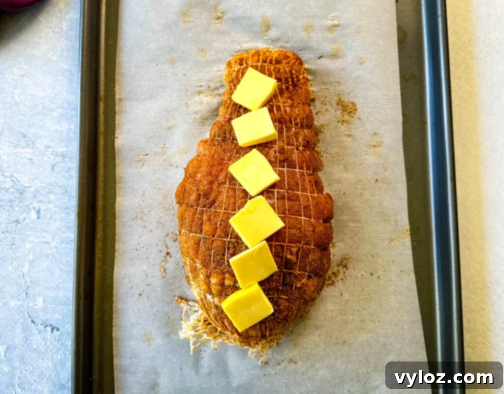 raw, seasoned boneless turkey breast topped with butter wrapped in a net on a parchment paper lined sheet pan