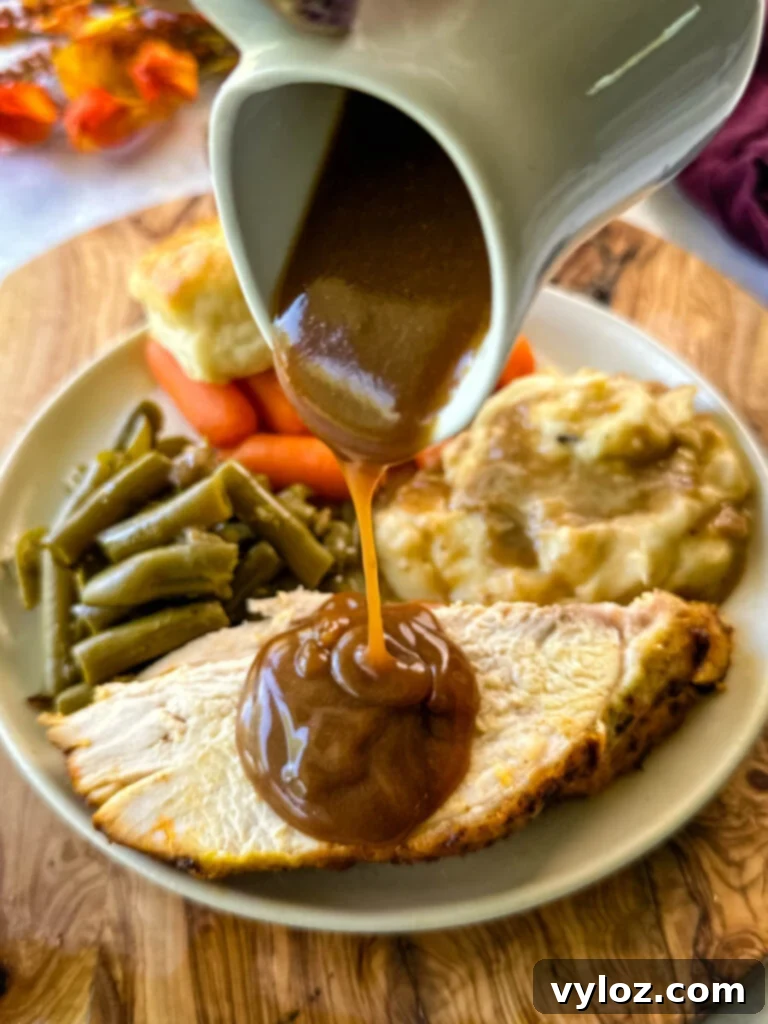 Juicy Bone-In Turkey Breast 2 gravy drizzled over sliced bone in turkey breast on a plate with mashed potatoes, green beans, carrots, and biscuits