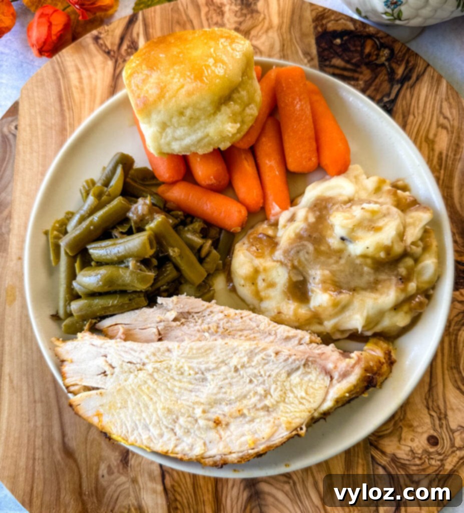 Juicy Bone-In Turkey Breast 13 sliced bone in turkey breast on a plate with gravy, mashed potatoes, green beans, carrots, and biscuits