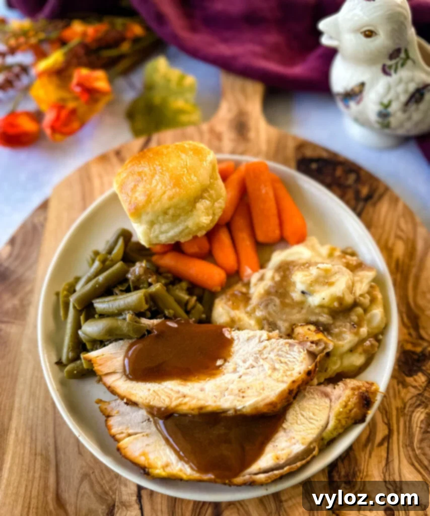 Juicy Bone-In Turkey Breast 14 sliced bone in turkey breast on a plate with gravy, mashed potatoes, green beans, carrots, and biscuits