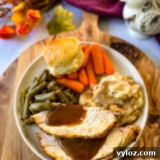 Juicy Bone-In Turkey Breast 15 sliced bone in turkey breast on a plate with gravy, mashed potatoes, green beans, carrots, and biscuits
