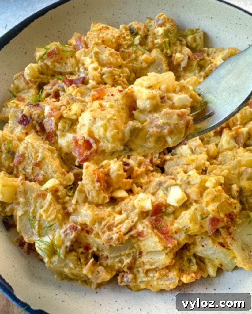 a fork full of bacon ranch potato salad over a white bowl