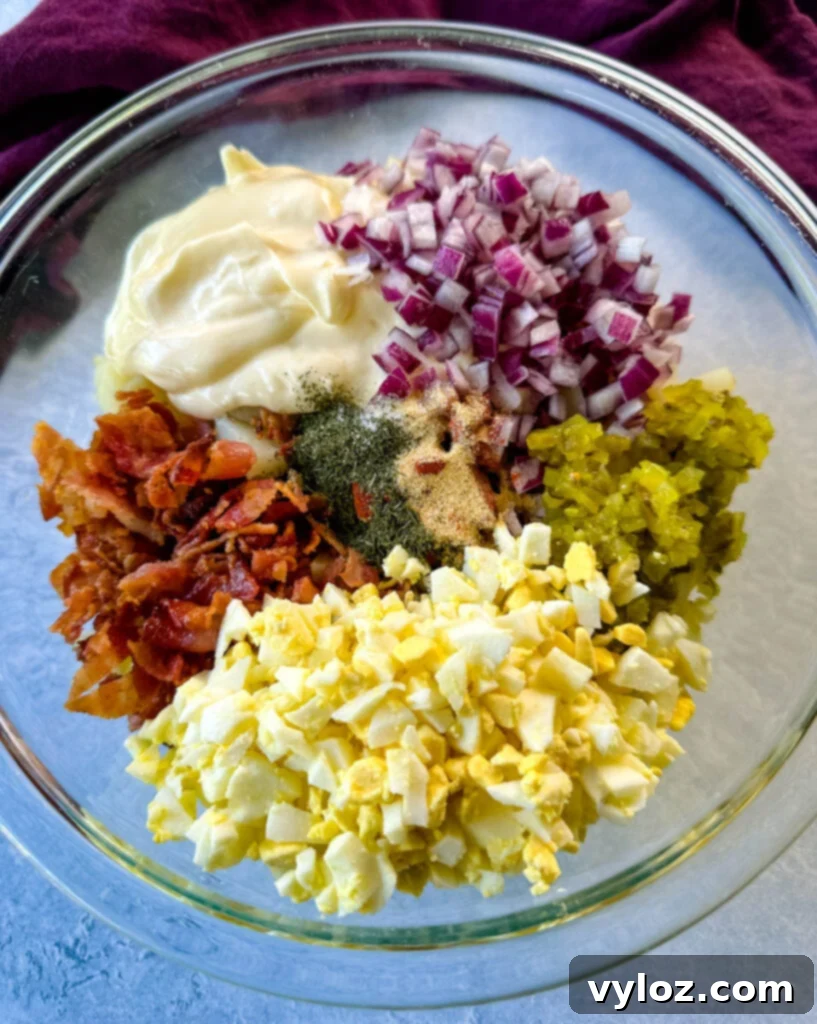 bacon pieces, onions, relish, diced hard boiled eggs, and ranch seasoning over potatoes in a glass bowl