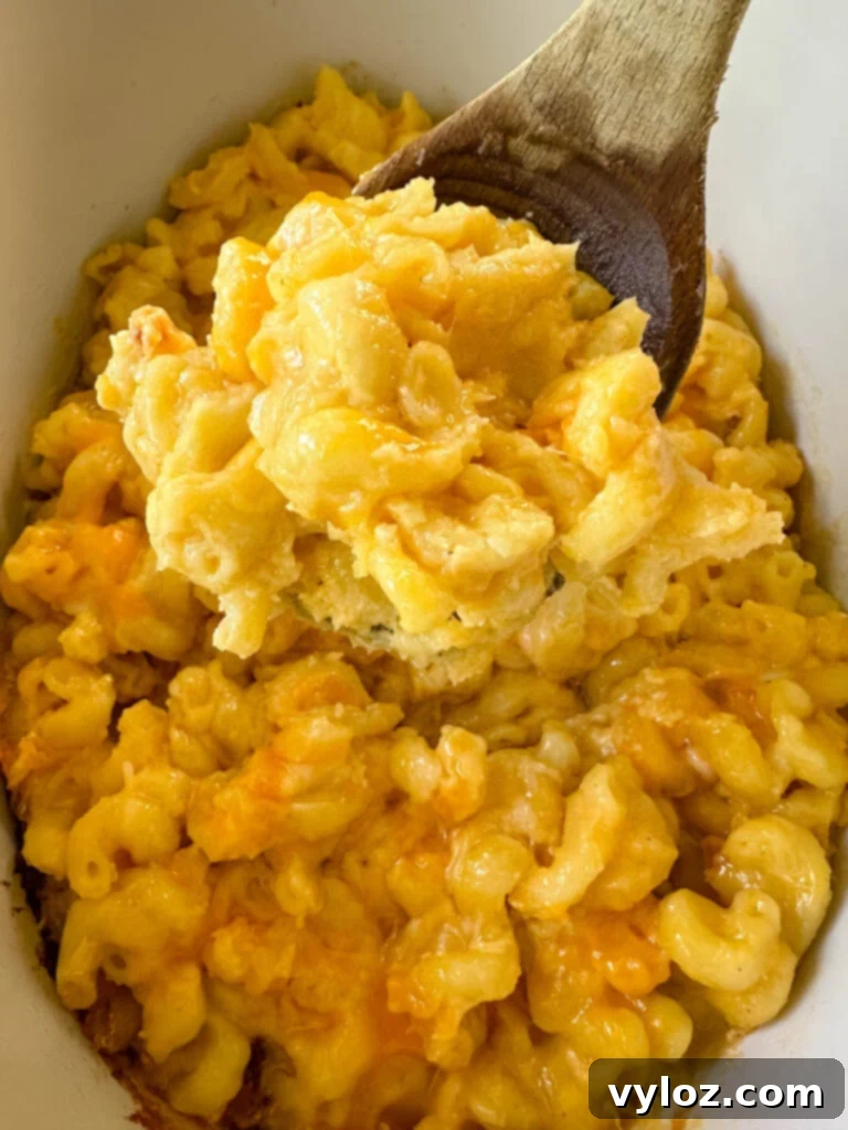 Effortless Crockpot Mac and Cheese 11 cheddar cheese mac and cheese in a Crockpot slow cooker with a wooden spoon